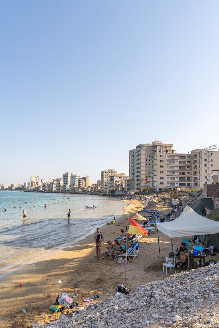 People enjoying a sunny day at Varosha Beach with tall buildings in the backdrop.